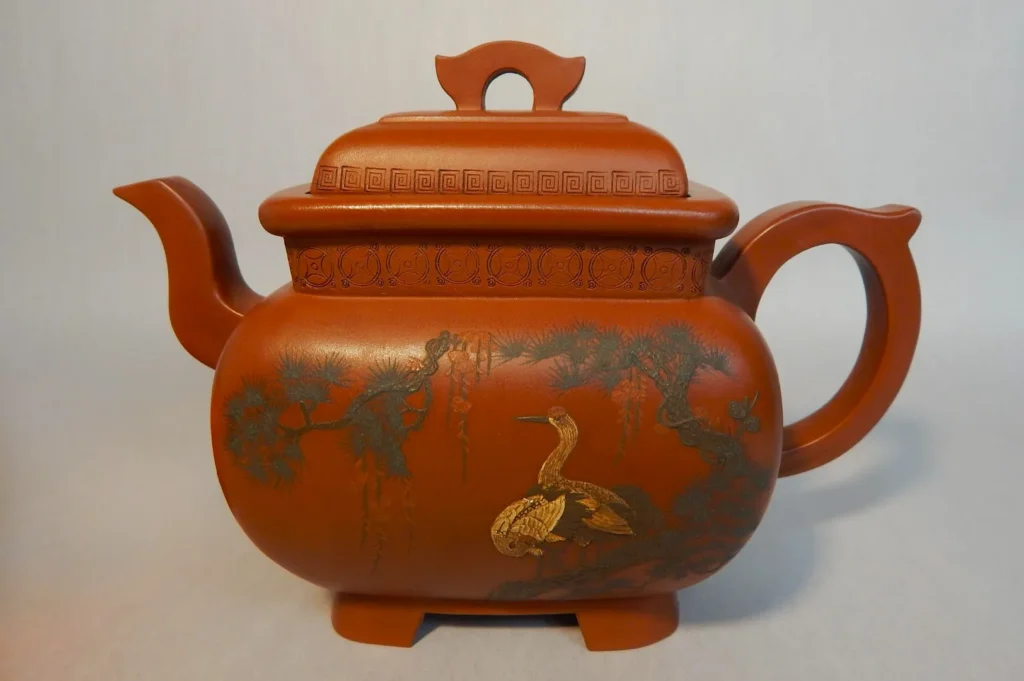 Brown clay teapot with intricate designs of a crane and trees, featuring elaborate handle and lid patterns. Elegant and artistic presentation.