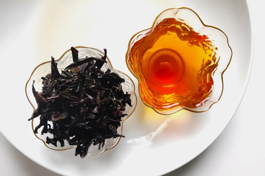 Two glass bowls are on a white surface. One contains dark, dried tea leaves; the other holds amber-colored brewed tea. The mood is calm and inviting.