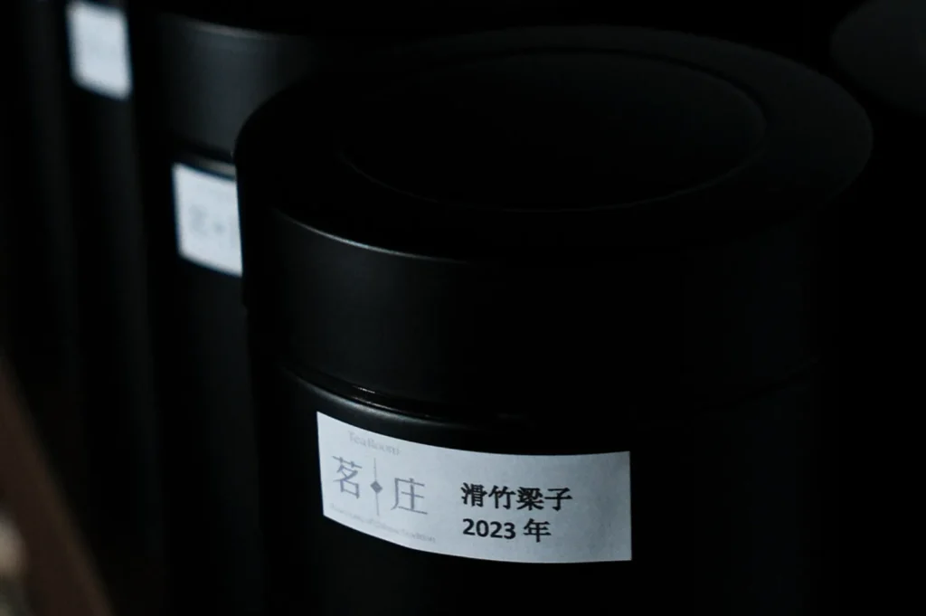 Close-up of a black tea canister with a white label showing Chinese characters and "2023." The scene is dimly lit, creating a calm, mysterious atmosphere.