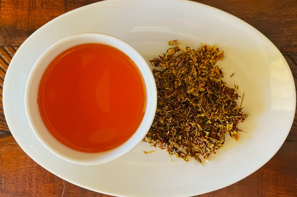 A white oval plate holds a cup of vibrant orange saffron tea and a small pile of dried saffron strands. The setting conveys warmth and luxury.