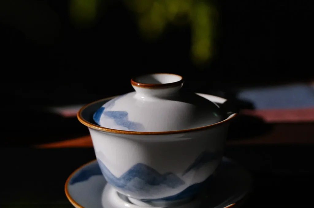 Elegant porcelain tea cup with subtle mountain design, accented by gold edges, sits in soft, dramatic lighting, conveying a serene, artistic ambiance.