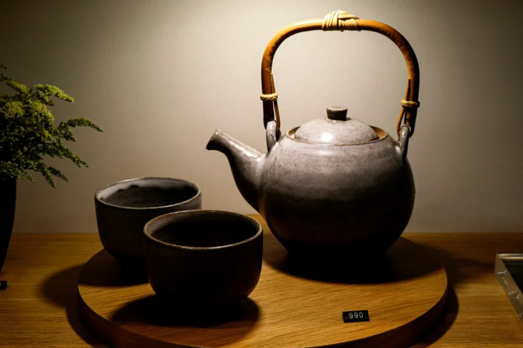 A gray ceramic teapot with a bamboo handle and two matching cups are displayed on a wooden tray. Soft lighting creates a warm, inviting atmosphere.