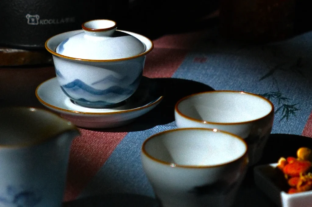 Elegant Chinese tea set with blue and white design in soft shadows. Three cups and lid on tray create a serene, intimate atmosphere.