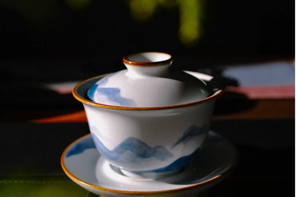 Ceramic tea cup and saucer with blue mountain design in soft light; evokes serenity and tradition, with focus on elegant, artisanal craftsmanship.