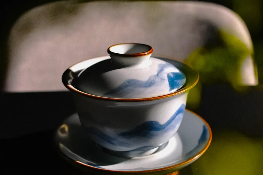 A porcelain teacup with a lid and saucer featuring blue wave patterns and orange rims, set against a dark background, evokes a serene, elegant mood.