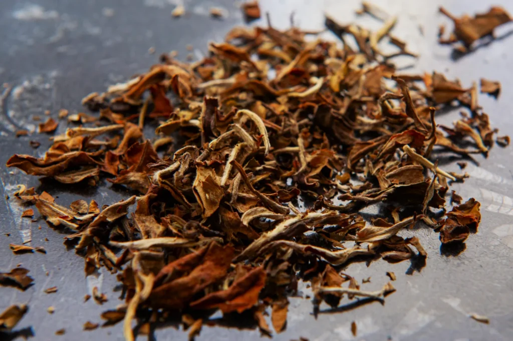 A pile of dried, loose-leaf tea, showcasing a variety of brown and earthy tones, is scattered on a smooth, dark surface, creating an organic texture.