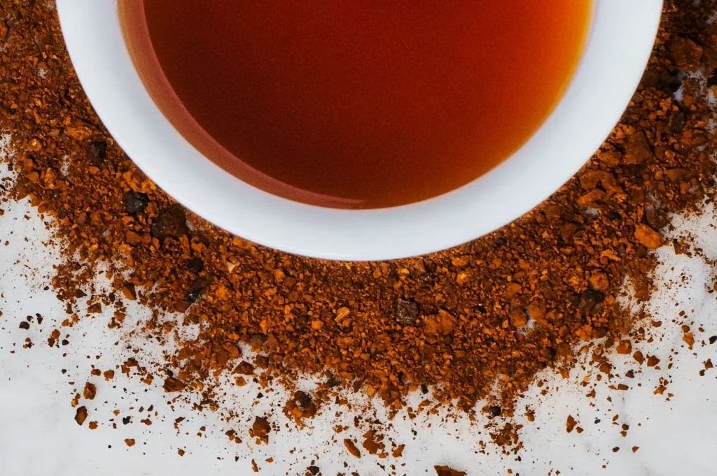A white cup filled with rich, amber tea sits on a marble surface, surrounded by scattered, aromatic coffee grounds, creating a warm, inviting contrast.
