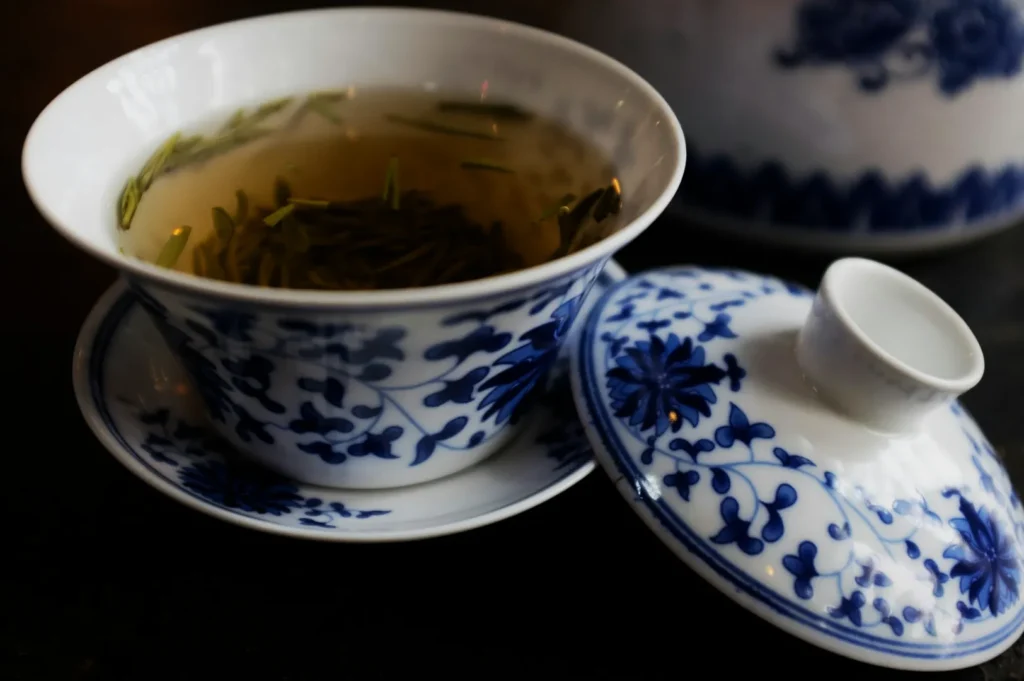 Elegant blue-and-white patterned porcelain tea cup with a lid, filled with brewed tea and floating leaves, on a matching saucer. Peaceful and refined.