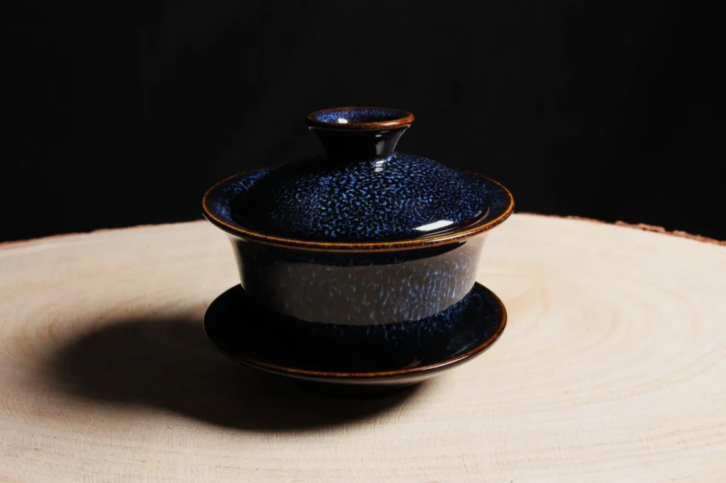 Elegant blue ceramic cup with lid on a wooden surface, against a dark background. The cup's glossy finish suggests sophistication and calm.