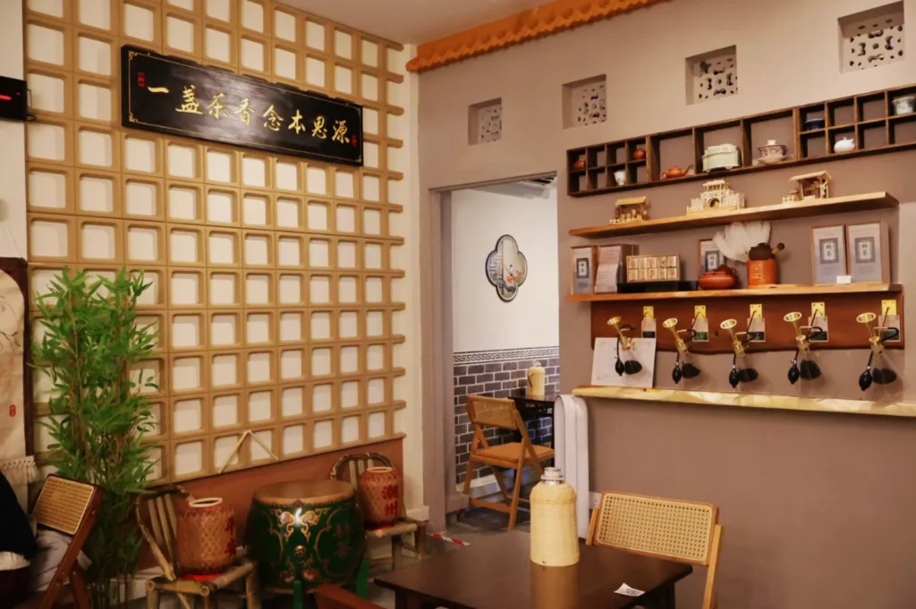 Cozy tea shop interior with bamboo decorations, wall shelves holding teapots, and a wooden counter with taps. Warm ambiance with earthy tones.