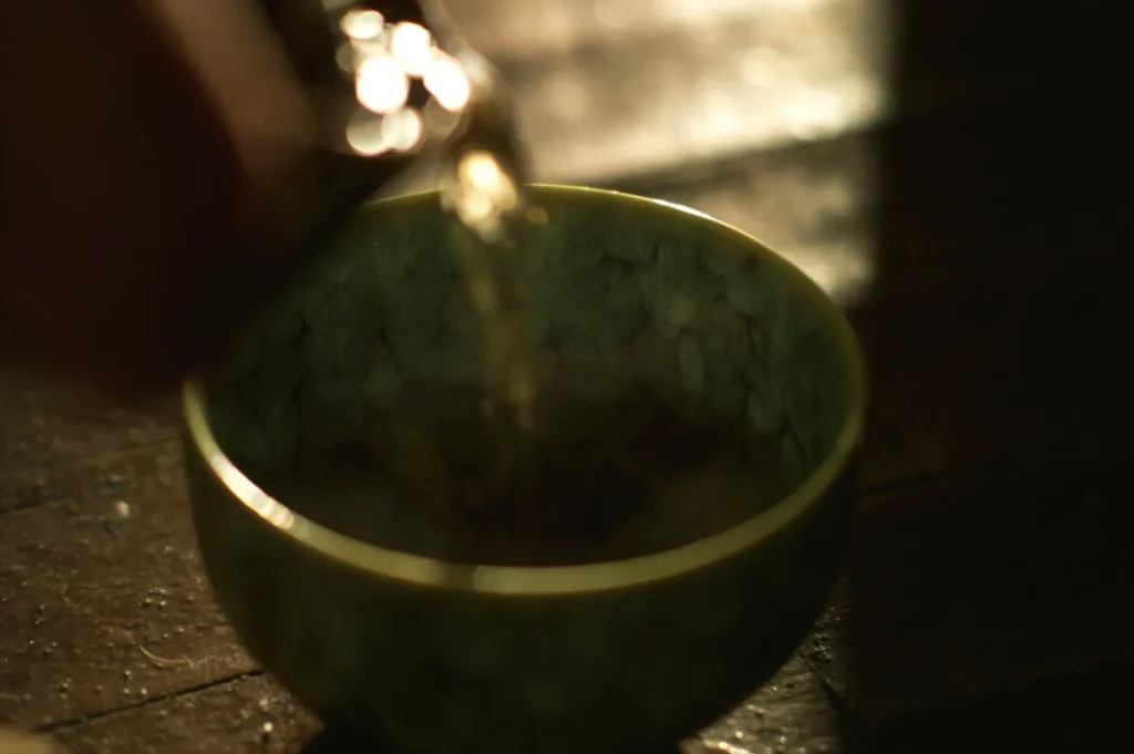 A warm, atmospheric image of a textured green ceramic cup on a wooden surface, with liquid being poured into it, creating a calm, serene mood.