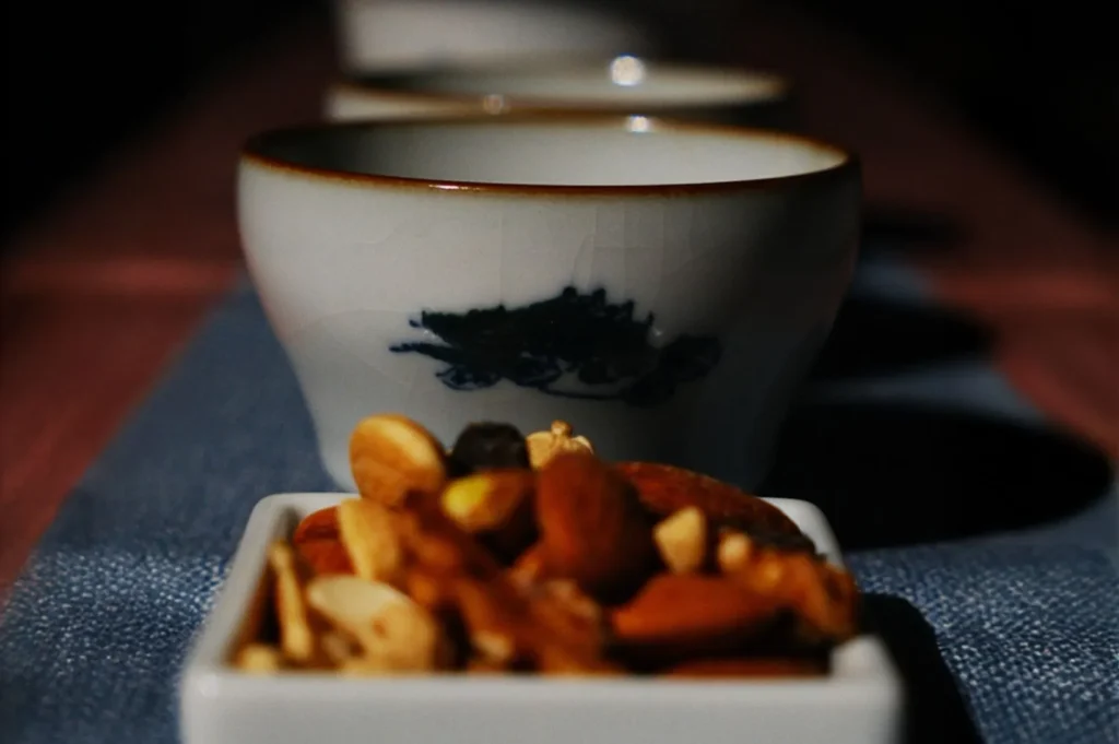 Close-up of white teacups aligned on a table, with a dish of assorted nuts in the foreground. The scene conveys a warm, inviting atmosphere.