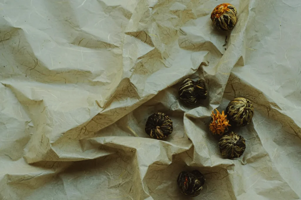 Dried flower buds scattered on crumpled, textured paper. The earthy tones and soft lighting create a natural, rustic, and serene atmosphere.
