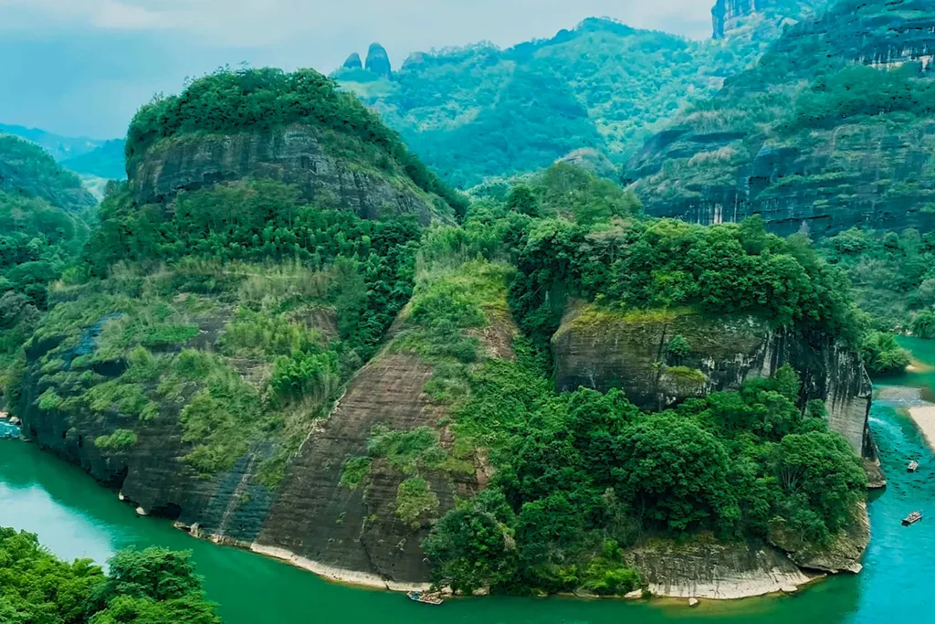 Lush, green mountain landscape with steep cliffs and dense foliage, surrounded by a winding turquoise river under a clear blue sky. Serene and captivating.