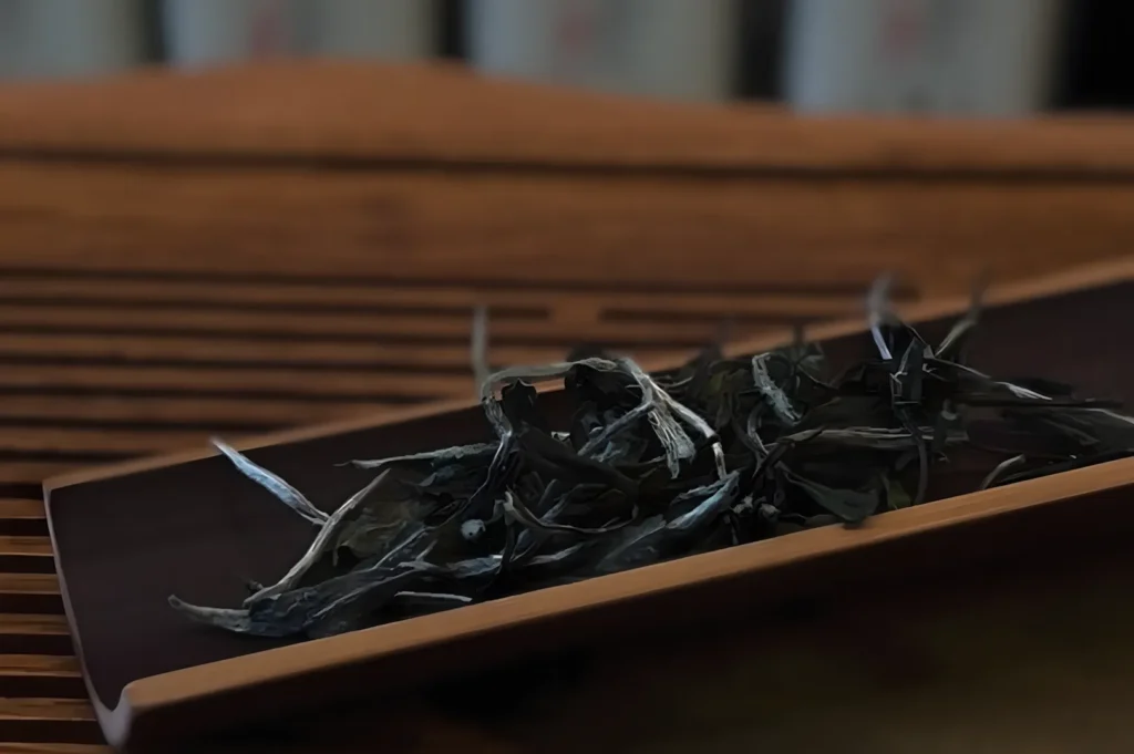 Dried tea leaves on a wooden tray, placed on a slatted table, convey a serene and earthy ambiance, suggesting a peaceful tea moment.