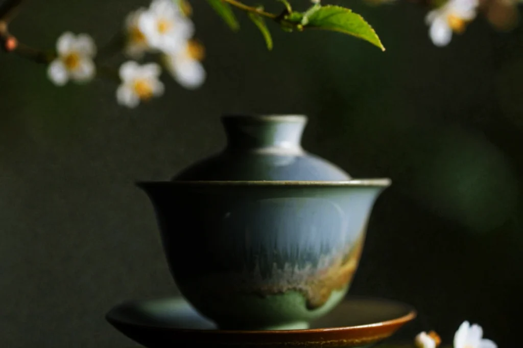 A serene, green ceramic teacup with a lid, set against a dark background and framed by soft-focus white blossoms, conveys tranquility.