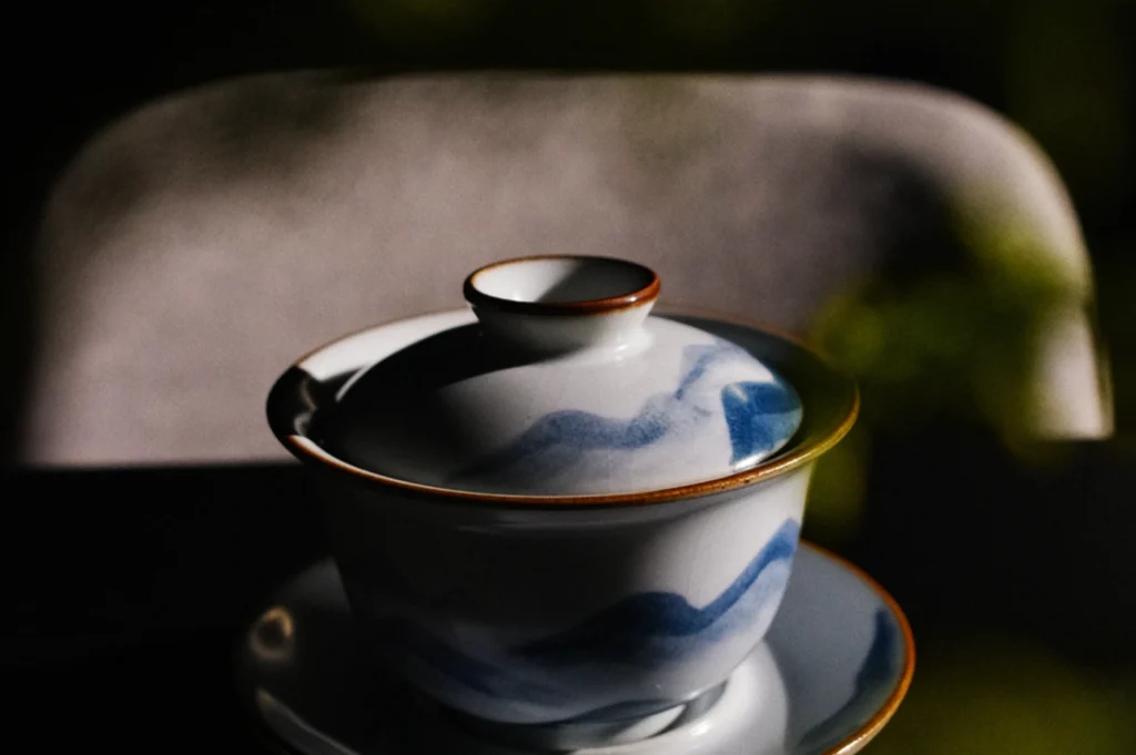 Elegant teacup with lid, blue wave design, sits on matching saucer. Soft lighting casts gentle shadows, evoking a serene, reflective mood.