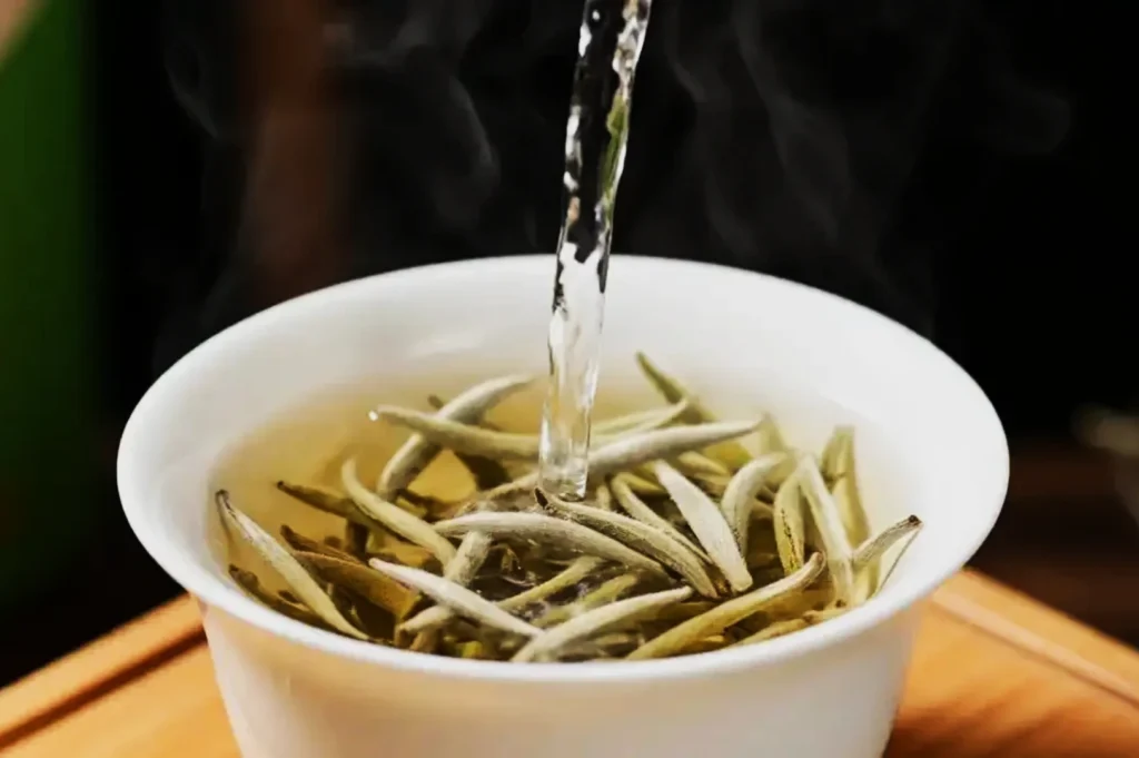 Pouring hot water over white tea leaves in a white cup, releasing steam. The scene feels calming and inviting, highlighting tea preparation.