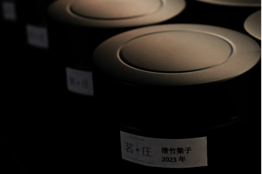 Rows of sleek, black tea canisters with Japanese labels, softly lit in dim lighting, conveying a sense of elegance and tranquility.