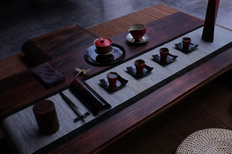 A beautifully arranged Japanese tea set on a wooden table with red cups and black plates on a runner. The setup conveys elegance and tranquility.