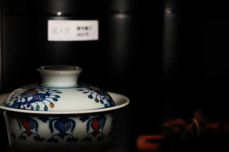 A detailed ceramic tea cup with vibrant blue and red intricate patterns sits against a dark backdrop, conveying an elegant and serene atmosphere.
