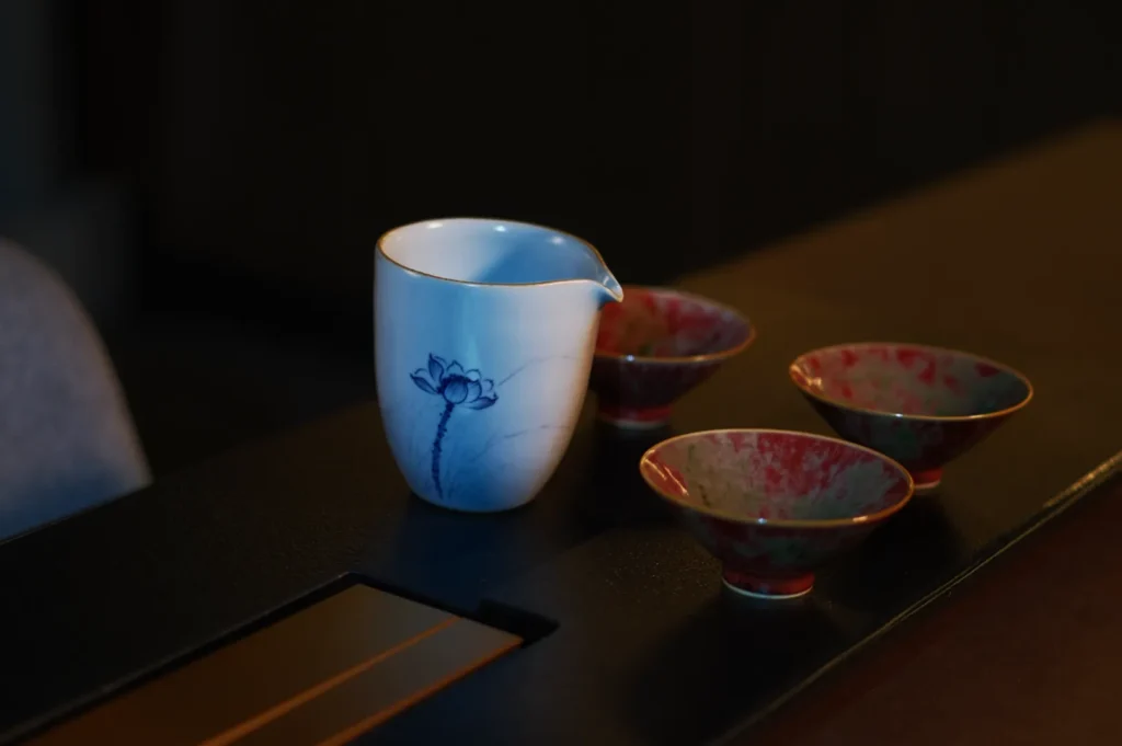 Ceramic pitcher with a blue floral design and three red speckled cups on a dark wooden table, creating a serene and elegant atmosphere.