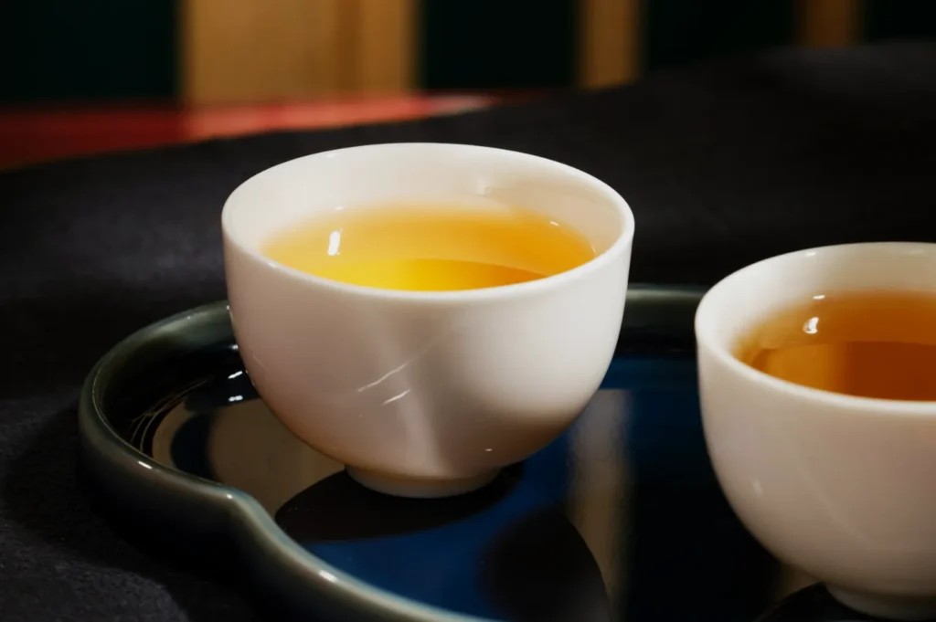 Two white ceramic teacups with golden tea sit on a dark blue, reflective tray. The scene is warm and inviting, evoking relaxation and calm.