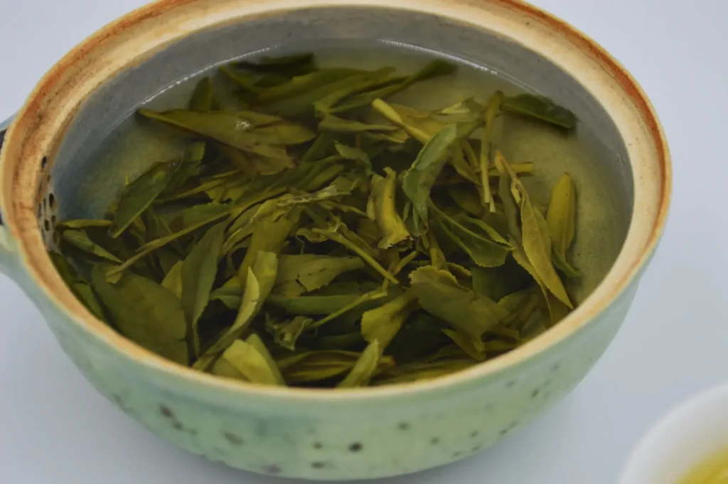 A close-up of a ceramic bowl filled with steeped green tea leaves in water. The bowl has a rustic feel, and the tone is calming and natural.