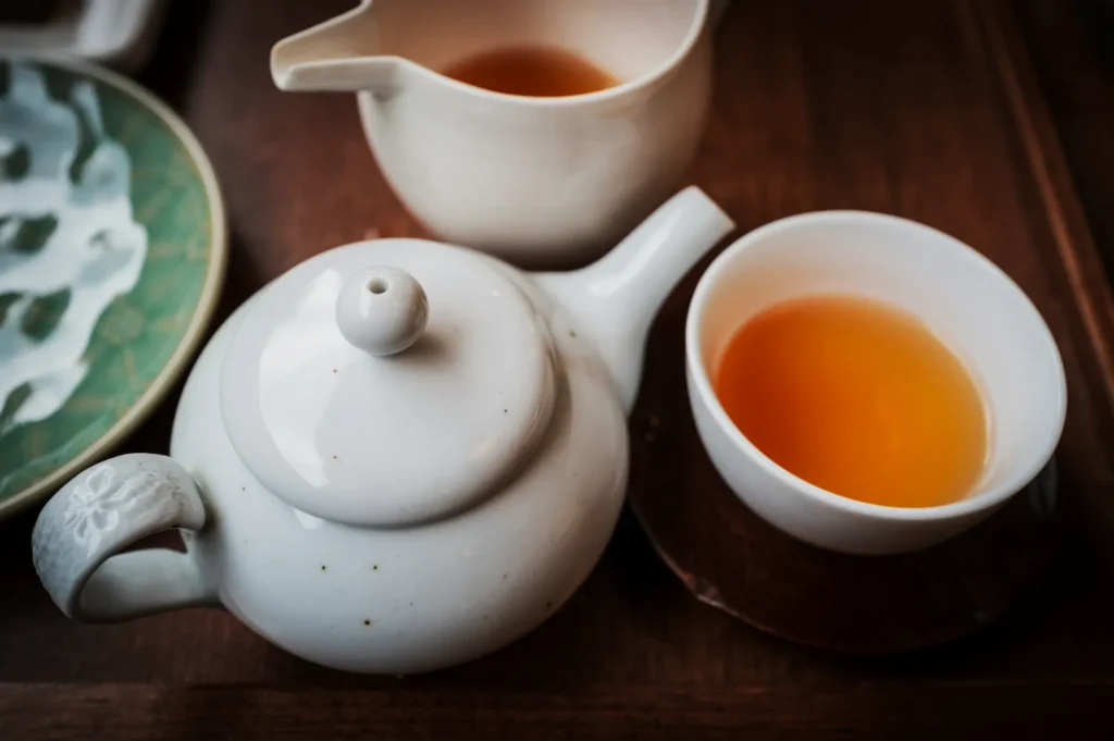 A serene tea setting with a white teapot, a cup, and a pitcher containing amber tea on a wooden tray. The mood is calm and inviting.