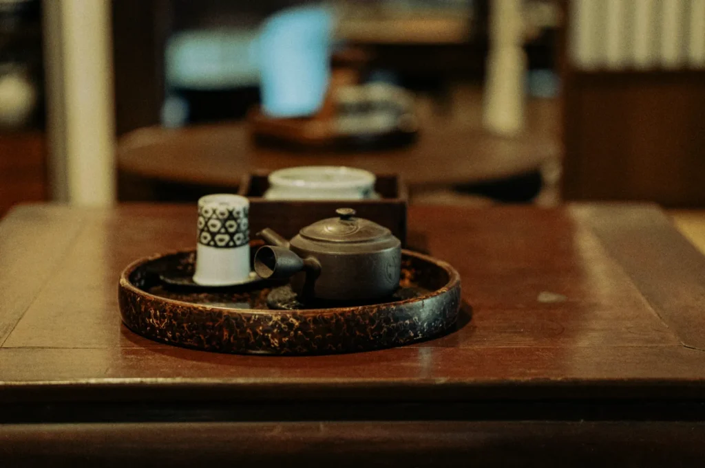 A rustic teapot and patterned cup sit on a round, wooden tray atop a polished table, evoking a cozy, traditional tea ceremony ambiance.