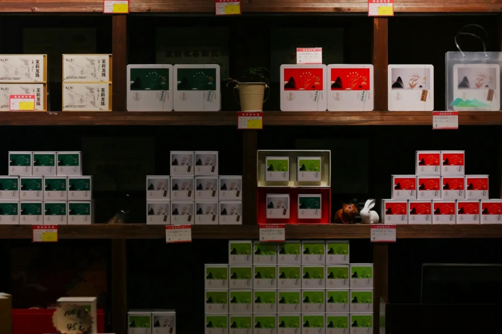 Dimly lit wooden shelves display neatly arranged boxes in red, green, and white. A small potted plant adds a touch of greenery.