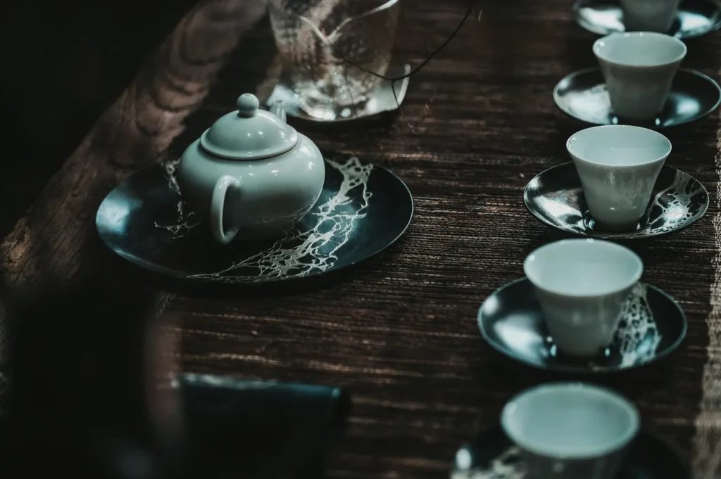 A serene tea setting with a white teapot on a dark, marble-patterned plate, surrounded by matching cups, arranged on a rustic wooden table.