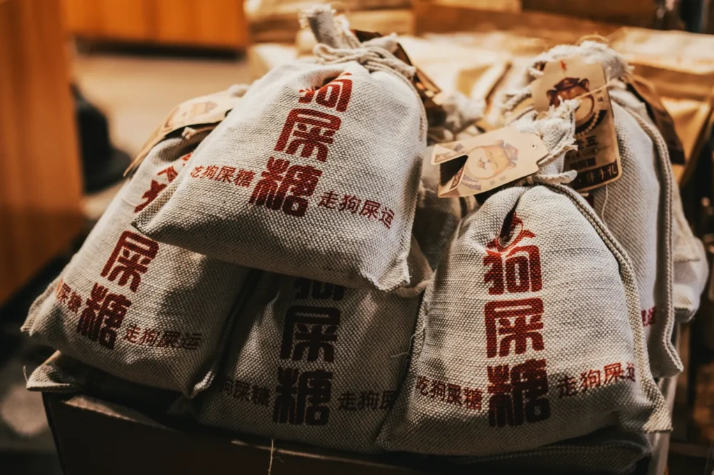 Burlap bags with red Chinese characters stacked in a pile, creating a rustic and traditional feel. Tags are attached, set against a warm background.