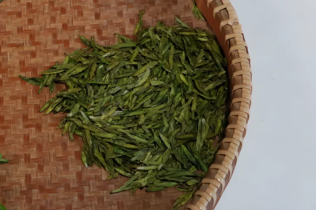 Close-up of green tea leaves in a round bamboo basket. The vibrant leaves are neatly spread, showcasing a natural, fresh, and organic texture.