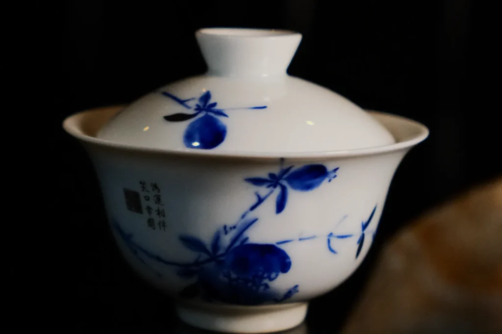 A white porcelain tea cup with a lid, adorned with blue floral motifs and Chinese calligraphy, conveys an elegant and traditional ambiance.
