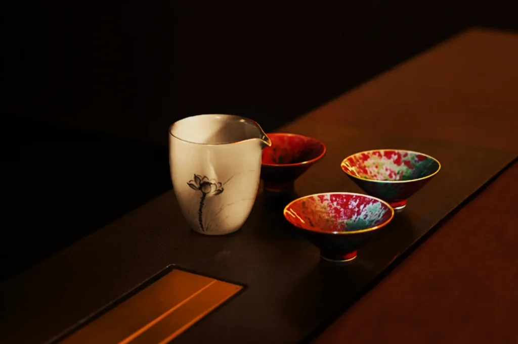 A white ceramic pitcher with a lotus design is flanked by three vibrant, multicolored bowls on a dark table, creating an elegant and serene atmosphere.