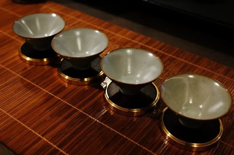 Four small, elegant teacups with gold rims sit in a row on a bamboo mat, creating a serene and traditional tea ceremony atmosphere.