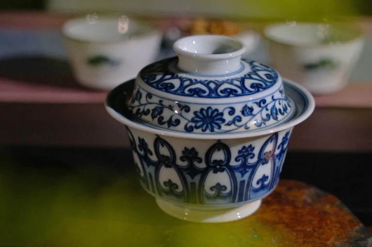 An ornate blue and white porcelain teacup with a lid, featuring intricate floral patterns, is centered. Two blurred cups are in the background.