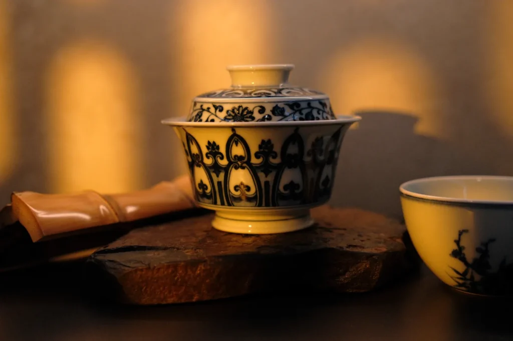 A porcelain tea set with intricate blue patterns sits on a stone slab, warmly lit by sunlight, creating a serene and elegant atmosphere.