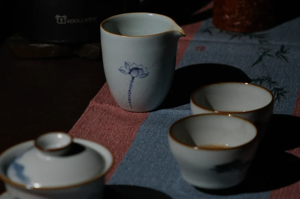 Ceramic pitcher and cups with blue floral designs sit on a textured, blue and pink tablecloth, creating a serene, traditional tea setting.