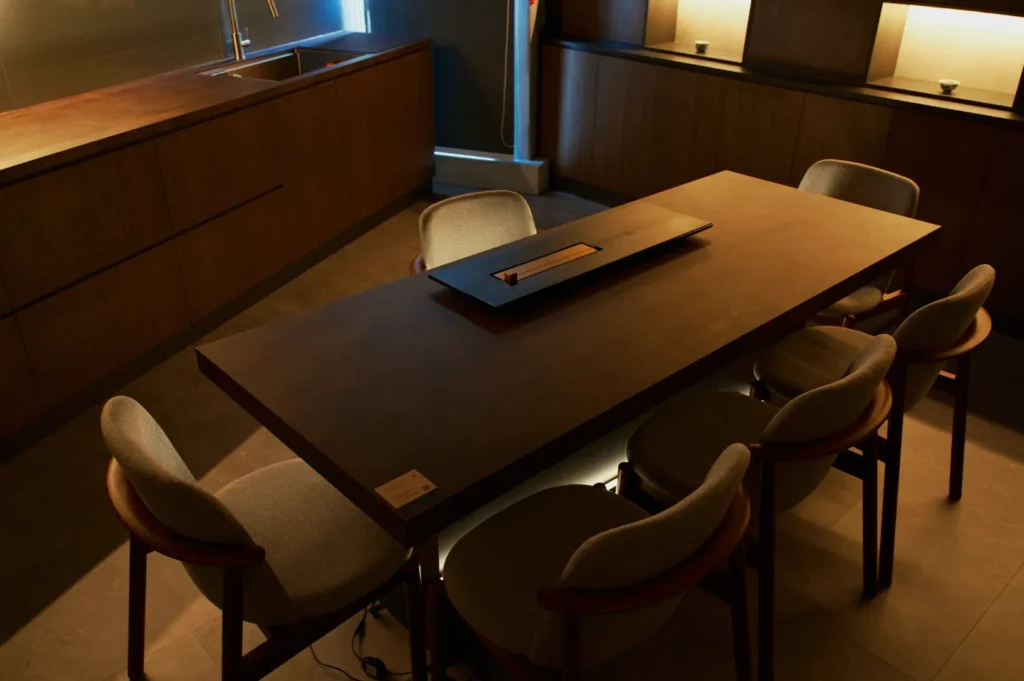 Modern dining room with a sleek wooden table and six upholstered chairs. Soft lighting creates a warm, minimalist, and inviting ambiance.