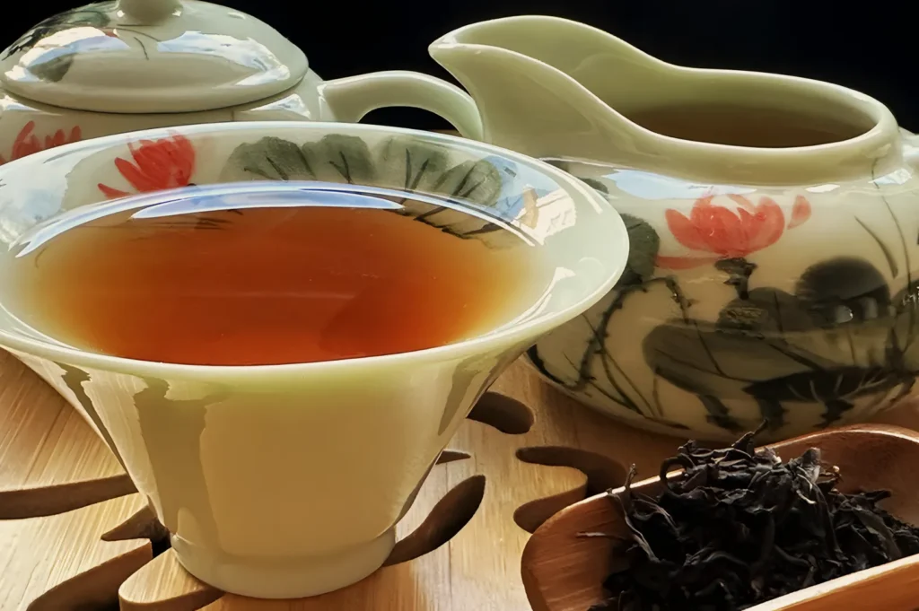 Elegant porcelain tea set with floral designs, filled with amber tea. Dry tea leaves rest on a wooden spoon, creating a serene and inviting atmosphere.