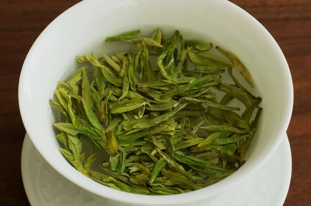 A white ceramic cup filled with green tea leaves soaking in water, creating a serene and calming scene on a wooden table.