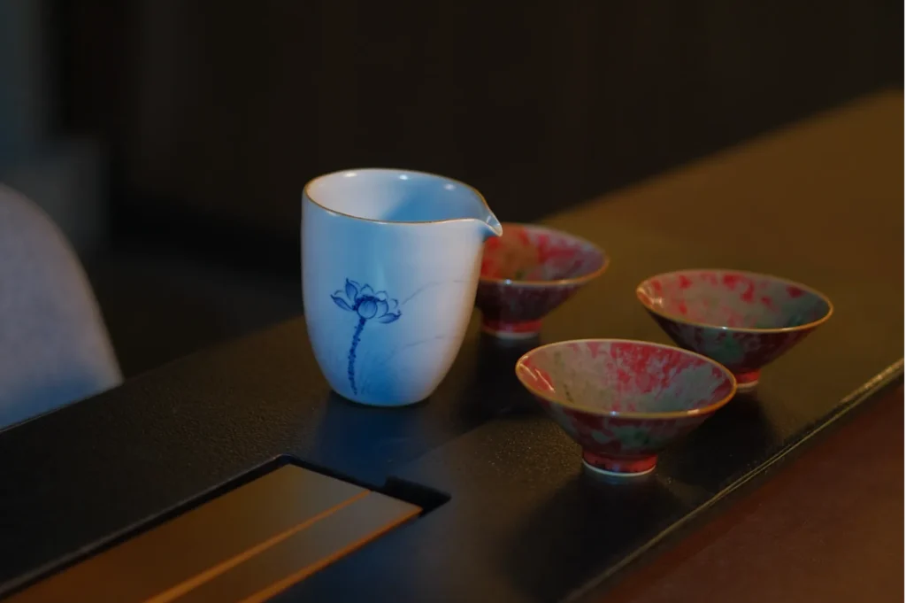 A delicate white pitcher with a blue floral design sits on a table, surrounded by three small red and green ceramic bowls, creating a calm and elegant atmosphere.