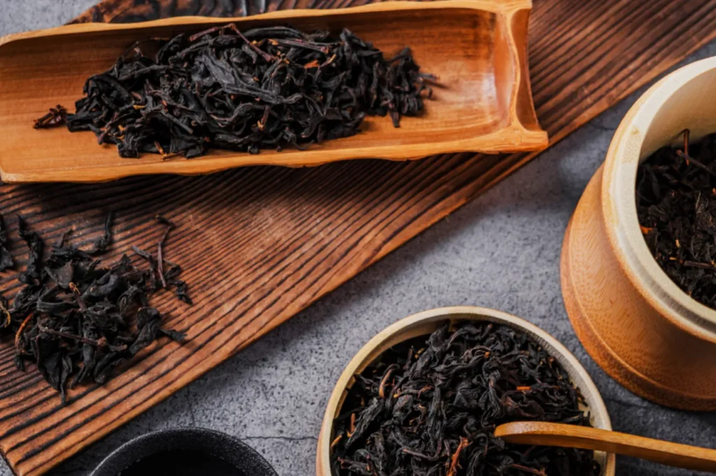 Assortment of loose black tea leaves displayed in wooden trays and bowls on a rustic surface, conveying a sense of warmth and traditional craftsmanship.