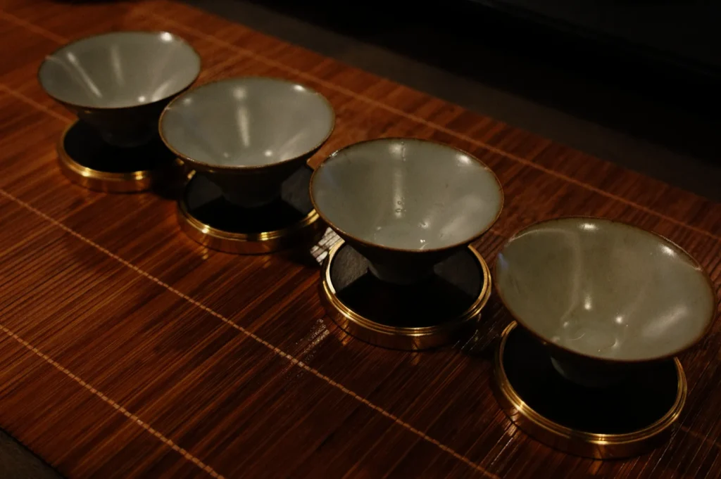 Four small ceramic bowls with golden bases are neatly arranged on a bamboo mat, creating an elegant and serene ambiance.
