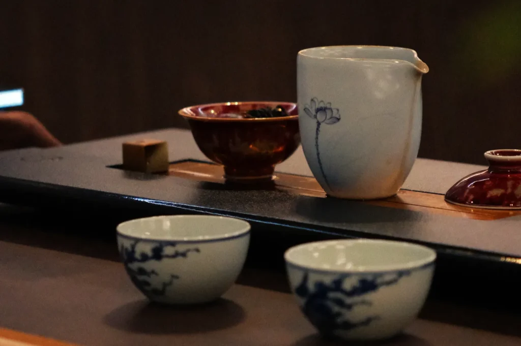 Elegant tea set on a dark tray including two white cups with blue floral designs and a pot with a lotus motif, evoking a serene ambiance.