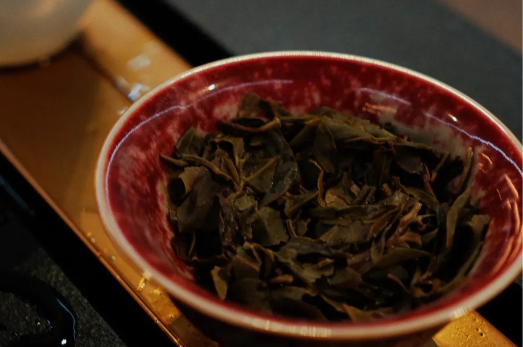 A close-up of a red bowl filled with dried tea leaves on a wooden surface, conveying a warm, earthy tone, perfect for a cozy tea moment.