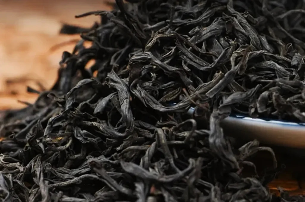 Close-up of a pile of dry, dark loose-leaf tea on a wooden surface, evoking a rich, earthy aroma and flavor, suggesting freshness and quality.