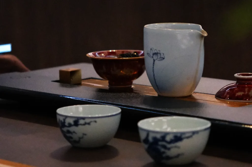 Ceramic tea set with two cups, a pot, and bowls on a tray. The pot has a floral design; the scene conveys a calm, traditional tea setting.